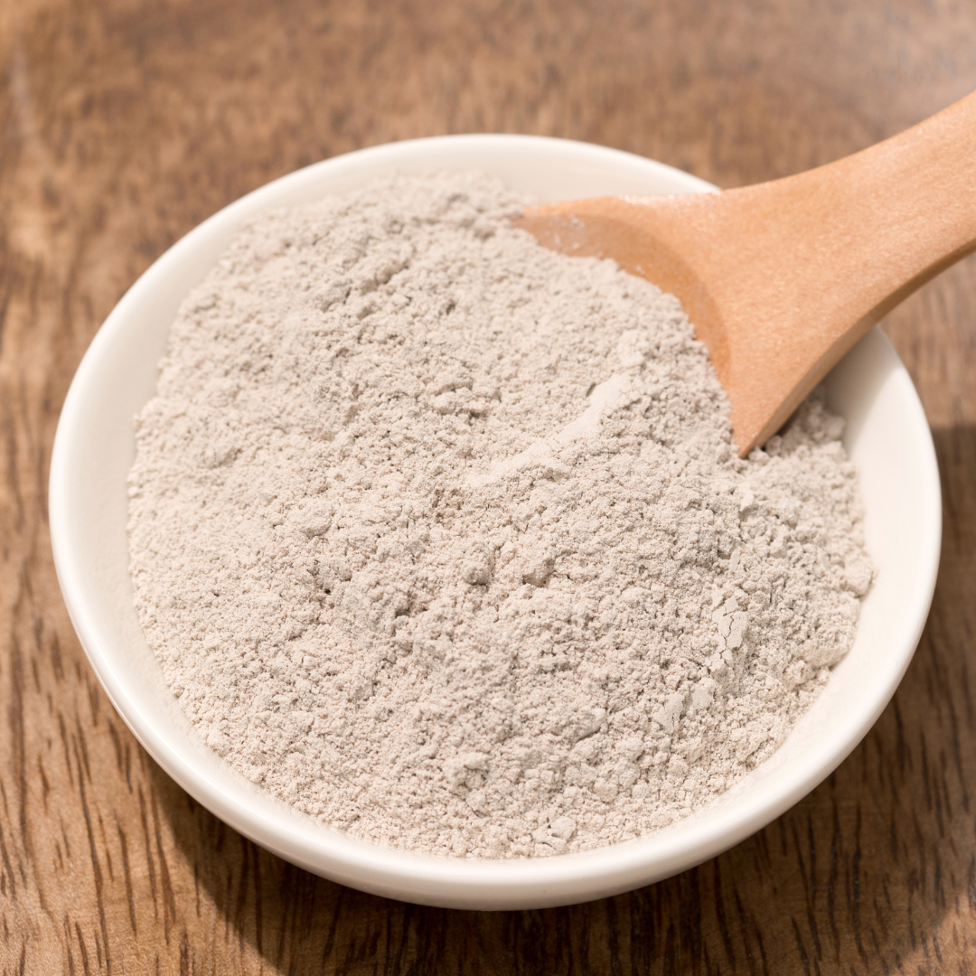 White bowl containing Bentonite Clay with a wooden bowl