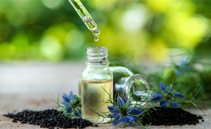 dropper hovering above bottle containing black seed oil, with nigella sativa seeds and flowers sitting on the surface around the bottle