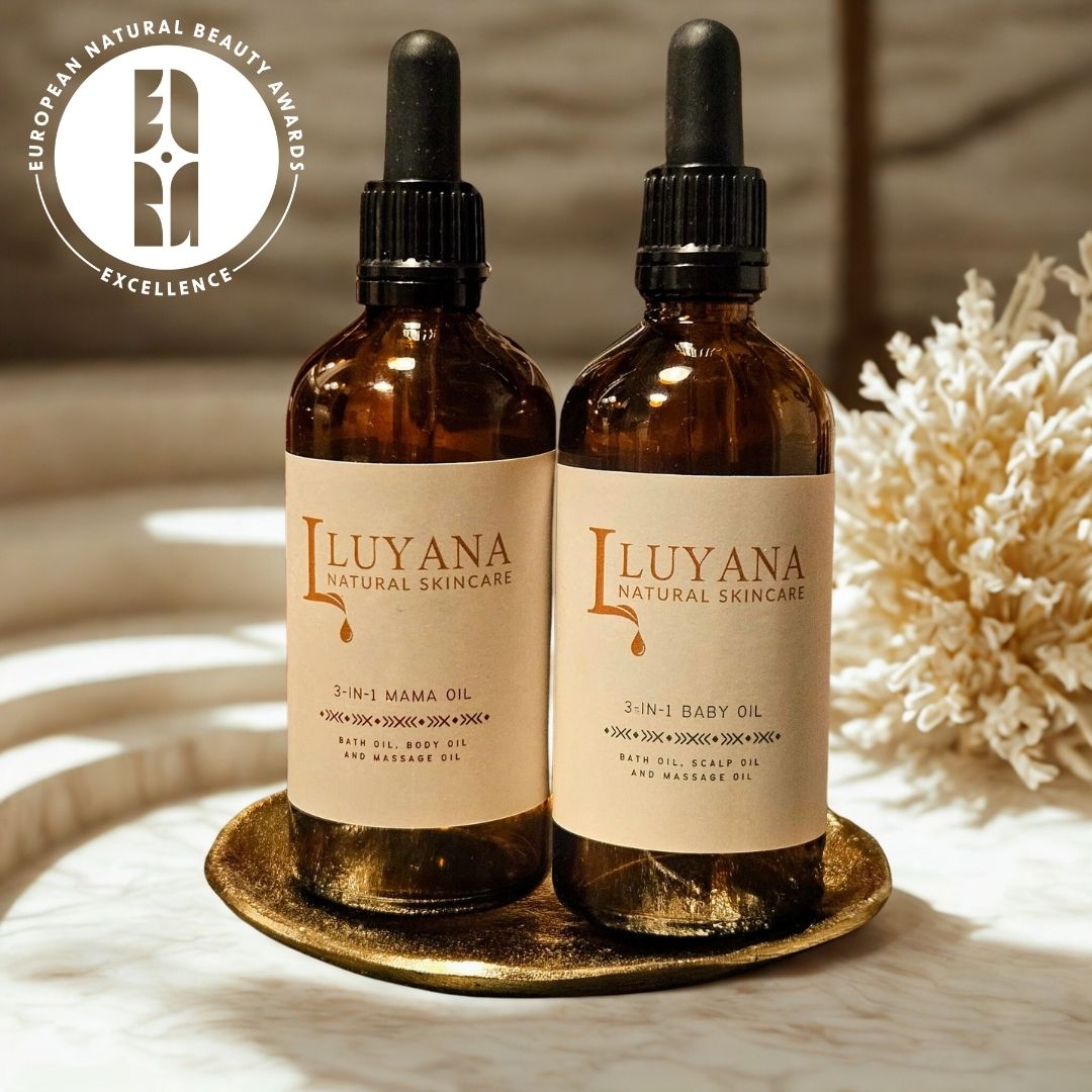 Two bottles of Luyana Natural Skincare (3-in-1 Mama Oil & 3-in-1 Baby Oil) on a decorative plate with a natural background, and a European Natural Beauty Award Excellence badge in the corner.