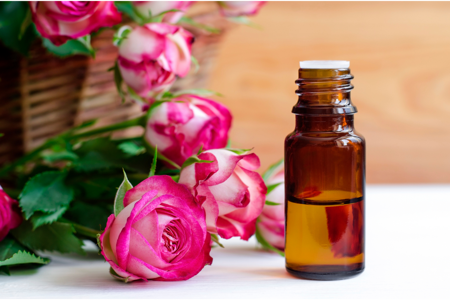 Small amber glass jar containing Rose Oil sitting next to pink and white roses